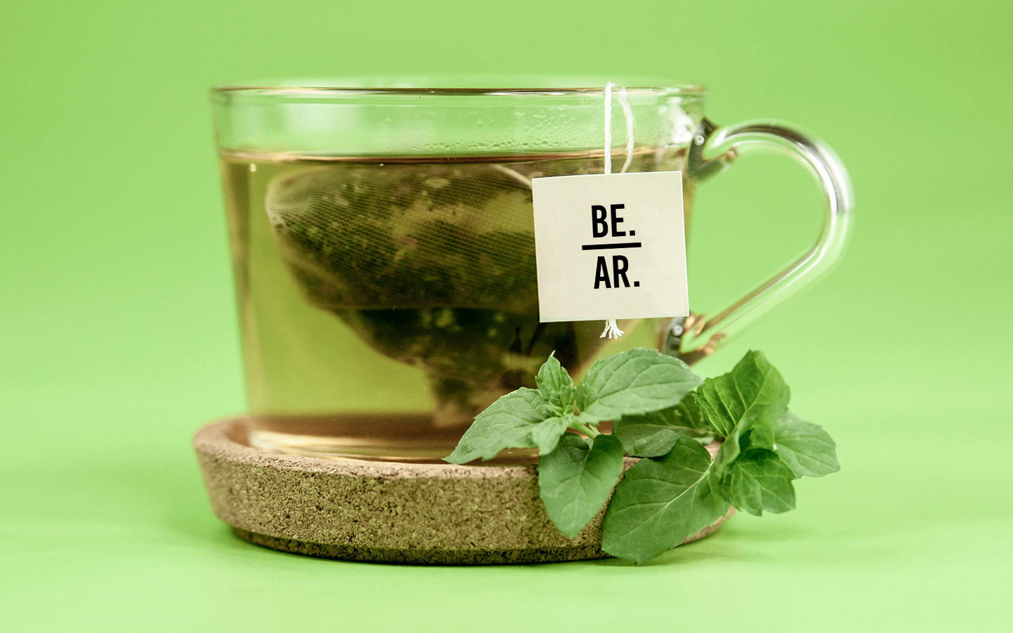 Clear glass mug with peppermint green tea and mint leaves on a green background