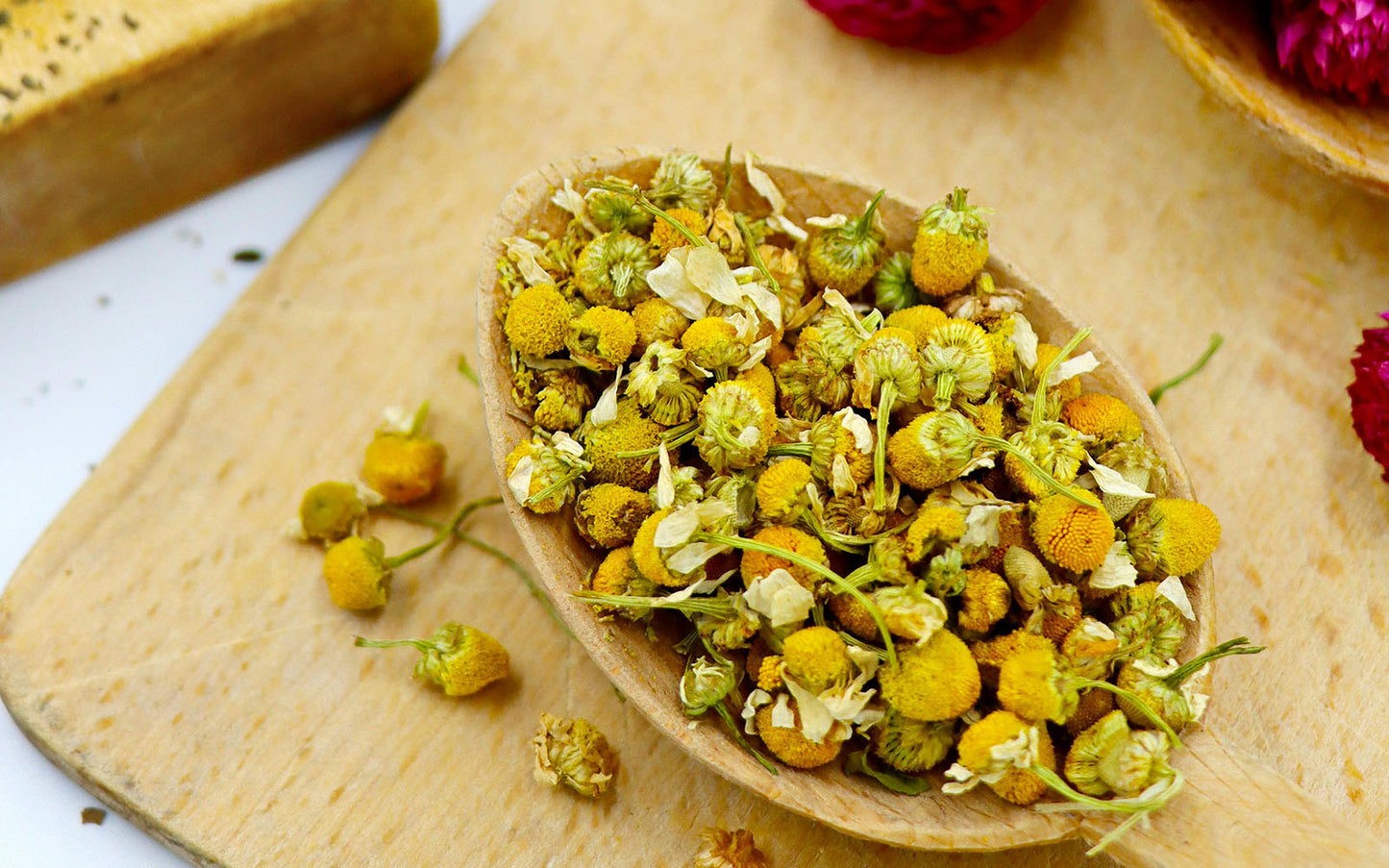 Dried chamomile flowers and herbs in a wooden spoon on a wooden platter
