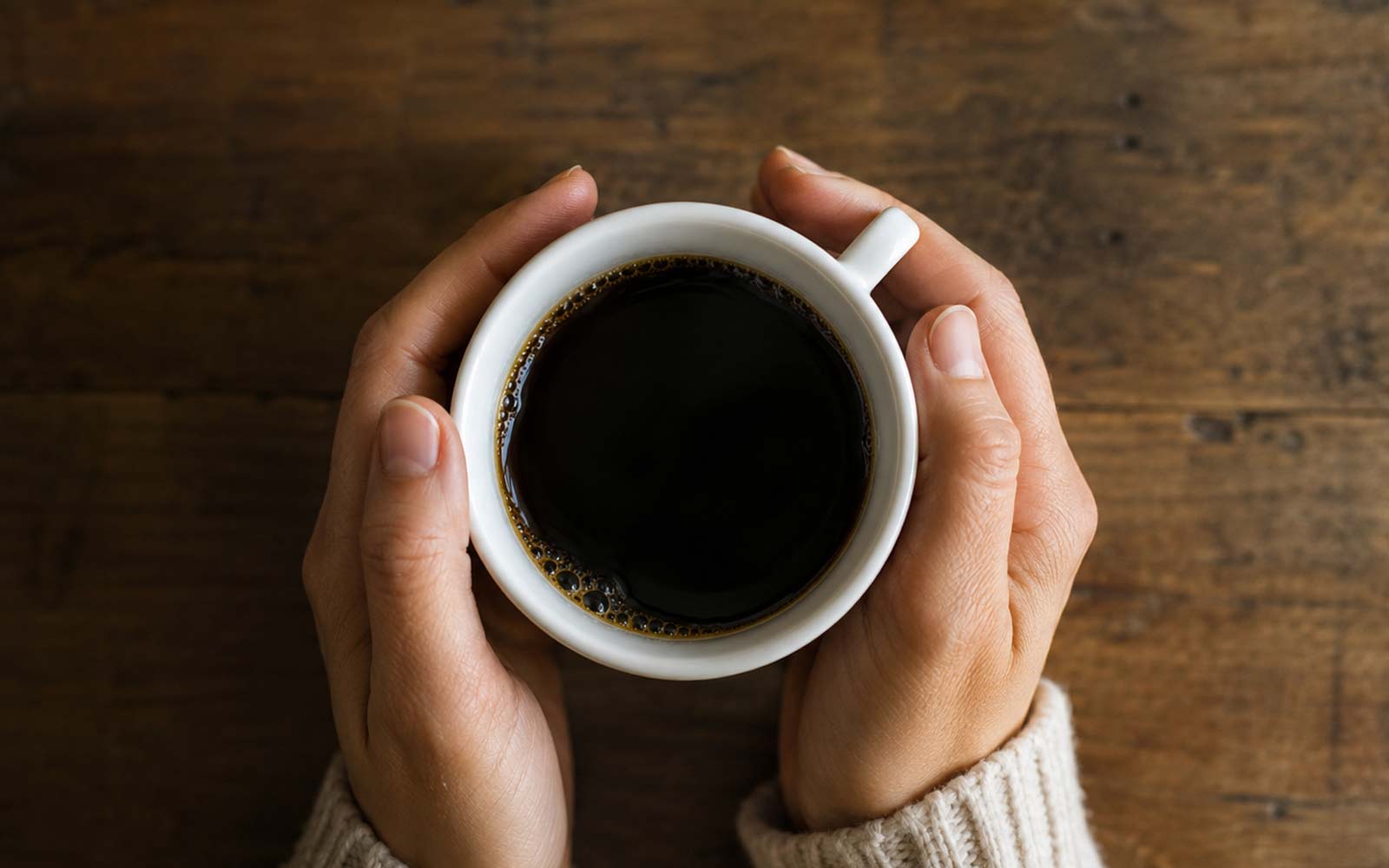 image of hands holding a bitter cup of black coffee, feature image for an article about how to fix bitter tasting coffee, and what the causes are. 