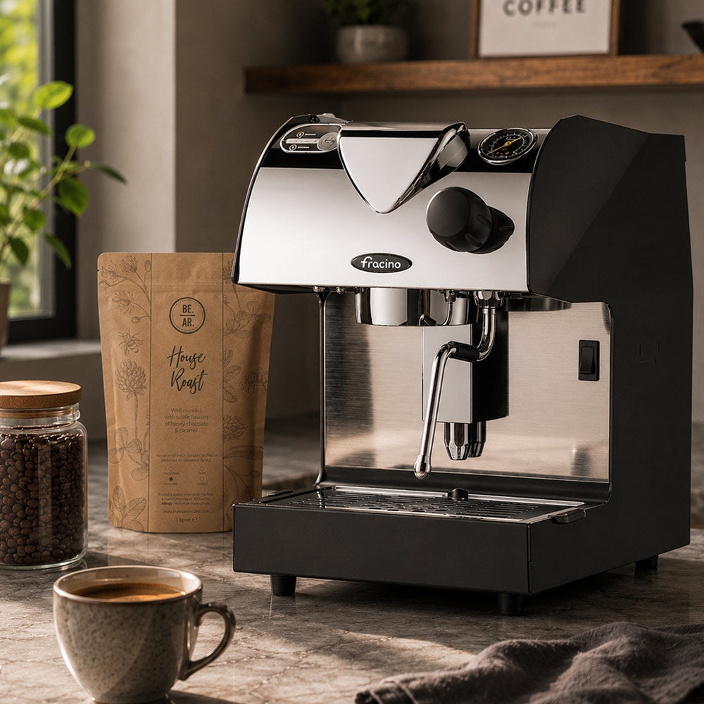 Black and stainless steel espresso machine by Fracino Piccino Home Espresso Machine - on a wooden table with a cup of coffee and coffee beans.