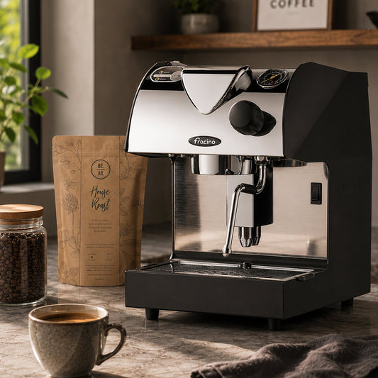Black and stainless steel espresso machine by Fracino Piccino Home Espresso Machine - on a wooden table with a cup of coffee and coffee beans.