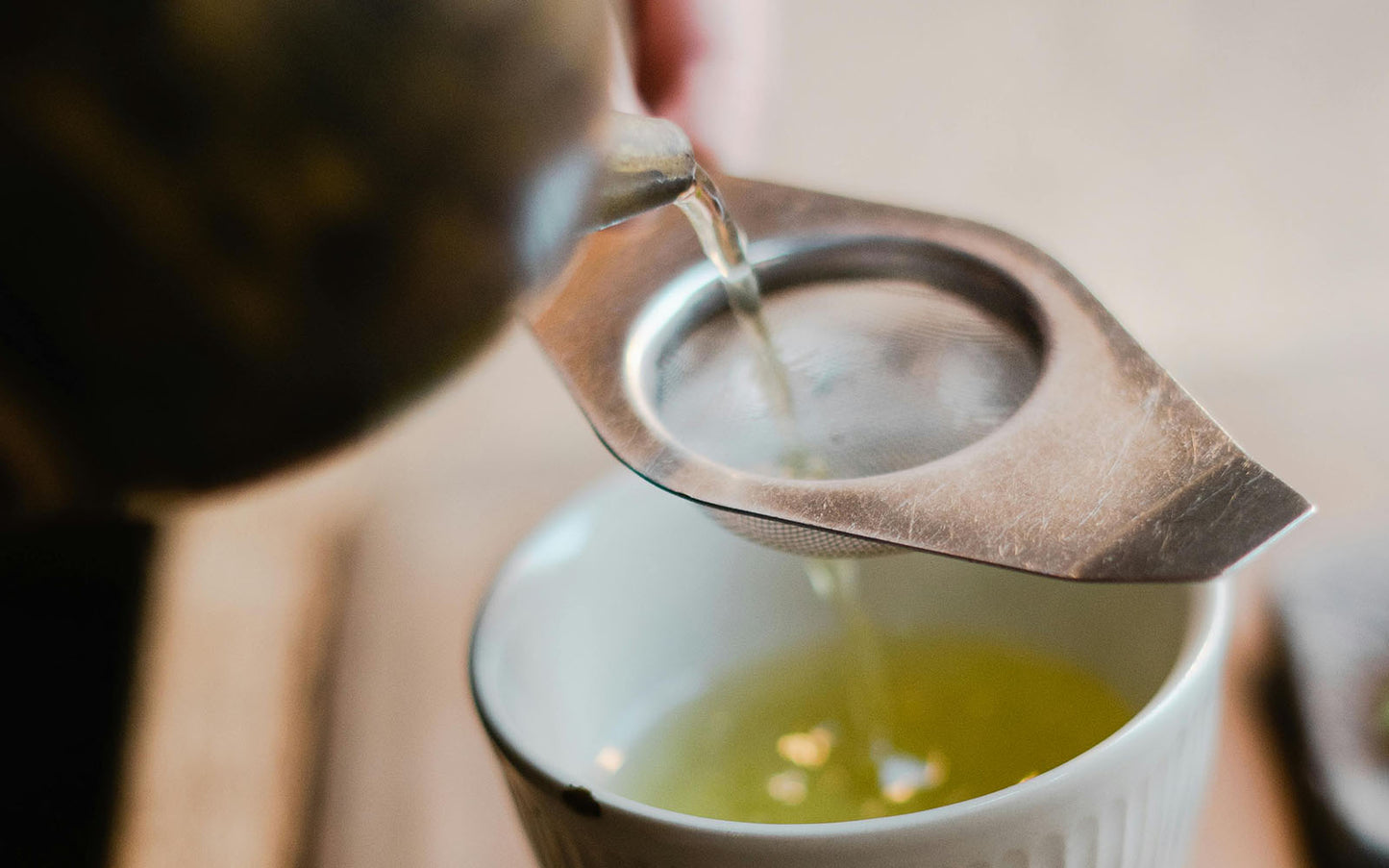 Japanese green sencha tea being poured from a teapot into a cup with a strainer.