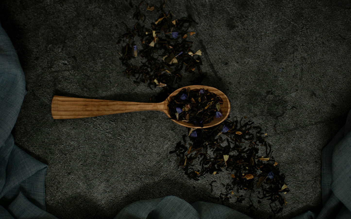 Wooden spoon filled with dried early grey tea on a dark textured surface
