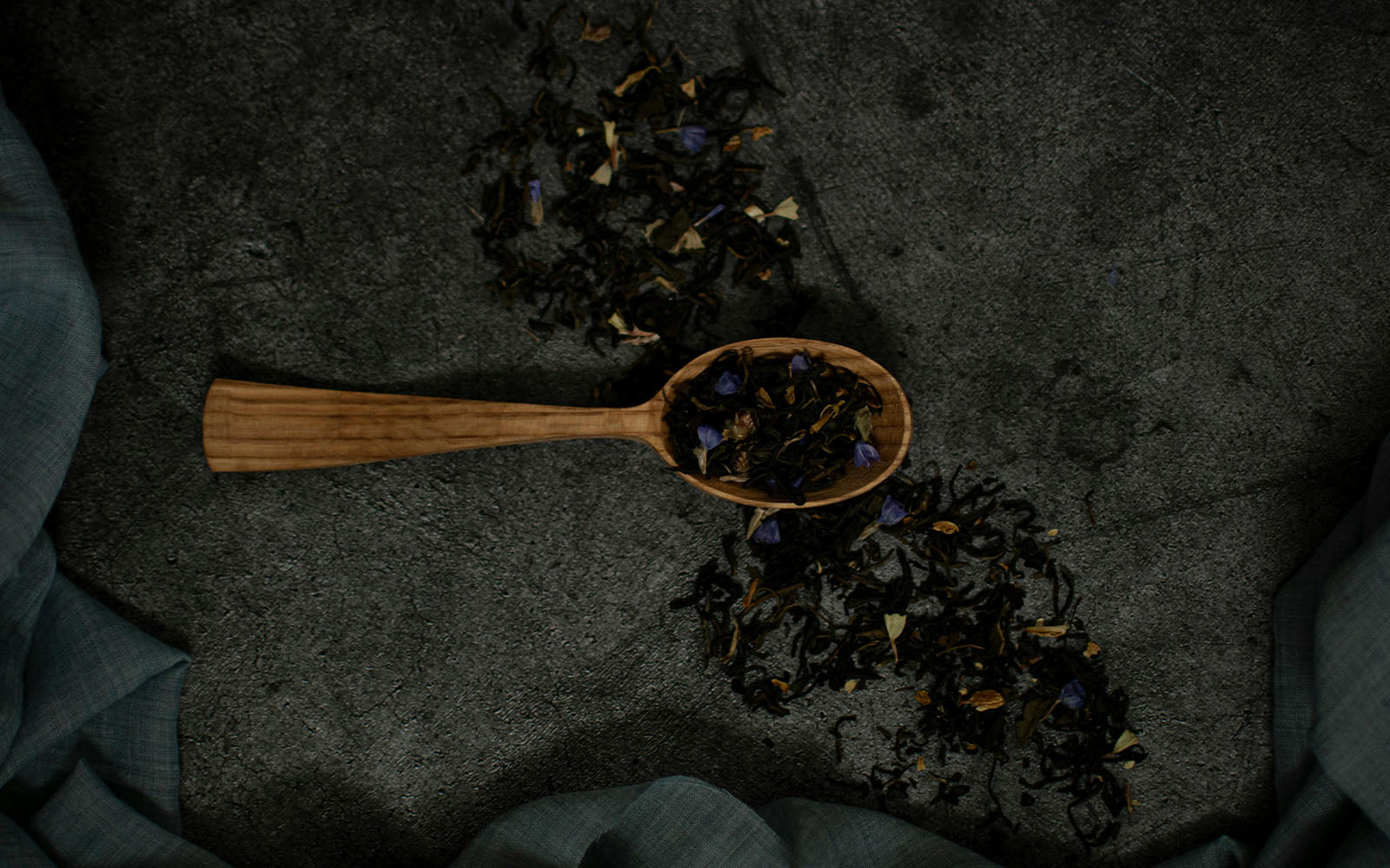 Wooden spoon filled with dried early grey tea on a dark textured surface